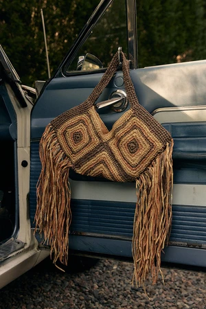 Crocheted fringe handbag hanging from the blue door handle of a vintage car outdoors