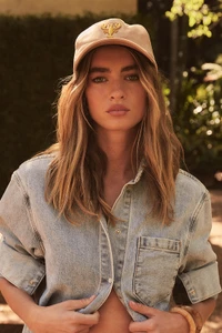 Woman in a light wash denim shirt wearing a tan cap with embroidered detail outdoors