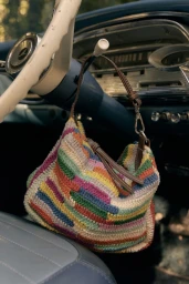 Colorful crocheted stripe handbag hanging from a vintage car steering column inside a classic automobile interior.