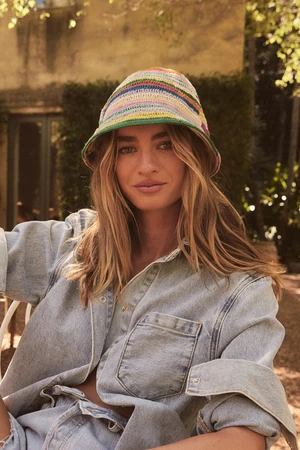 Woman wearing a multi-coloured striped crochet bucket hat and denim shirt outdoors in front of a building exterior