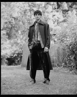 Model Noel Hernandez wearing a long coat and velvet trousers outdoors in a black and white portrait for Numéro Homme Netherlands.