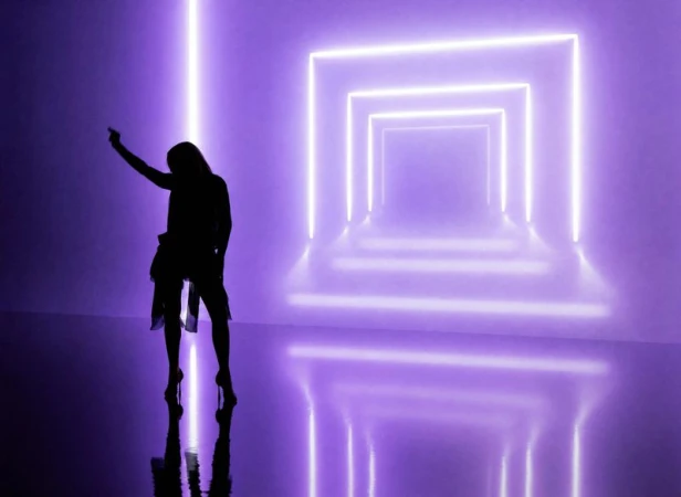 Silhouette of Madonna posing in high heels in front of glowing purple neon rectangular frames on a reflective studio floor.