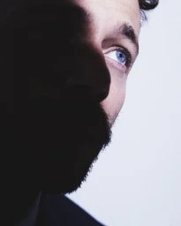 Close-up portrait of Ludovico Tersigni in shadow with striking blue eyes against a white background by Simone Paccini