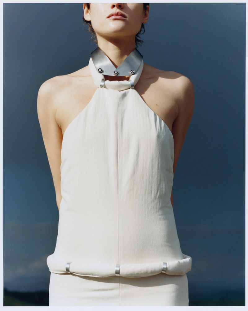 Model wearing a cream halter top with an industrial metallic collar against an overcast sky.
