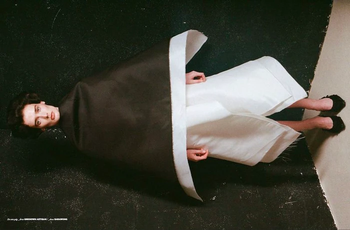 Model wearing sculptural black and white structured dress lying on a dark textured background for Issue South America