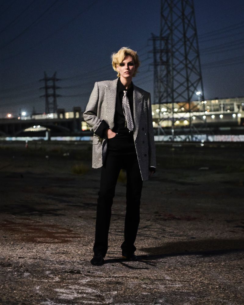 Vittoria Ceretti wearing an oversized silver blazer, patterned tie, and black trousers at night against power lines.
