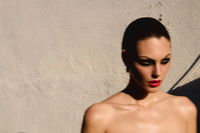 Close-up portrait of model Vittoria Ceretti with dark hair, bold eye makeup, and bright red lipstick against a textured wall