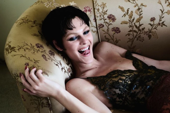 Model Vittoria Ceretti reclining on a vintage floral patterned sofa wearing a dark lace top for Vogue Italia