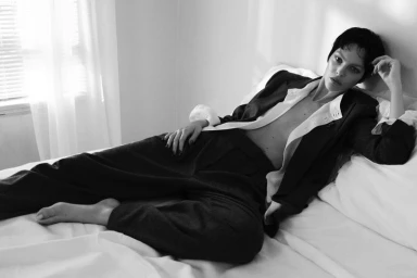 Model Vittoria Ceretti reclining on a bed in tailored trousers and jacket for Vogue Italia