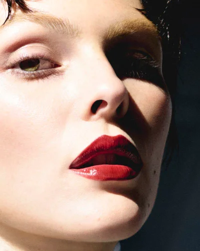 Close-up beauty portrait of Vittoria Ceretti with bold red lipstick and bleached eyebrows under direct hard lighting.