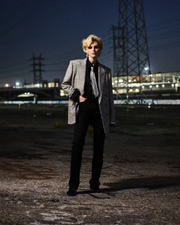 Vittoria Ceretti wearing an oversized silver blazer, patterned tie, and black trousers at night against power lines.