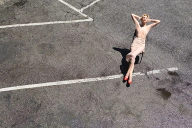 Vittoria Ceretti sits on a chair with arms behind her head on an asphalt parking lot marked with white painted lines.