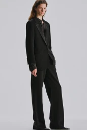 Sandra Murray wearing a tailored black suit with wide-leg trousers and a black blazer against a light grey studio background.
