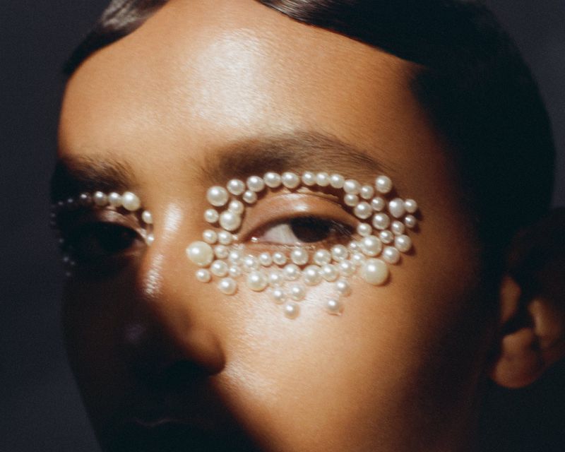 Close-up of a woman's face with pearls around her eyes, highlighting beauty and fashion elements in a studio setting with soft lighting.