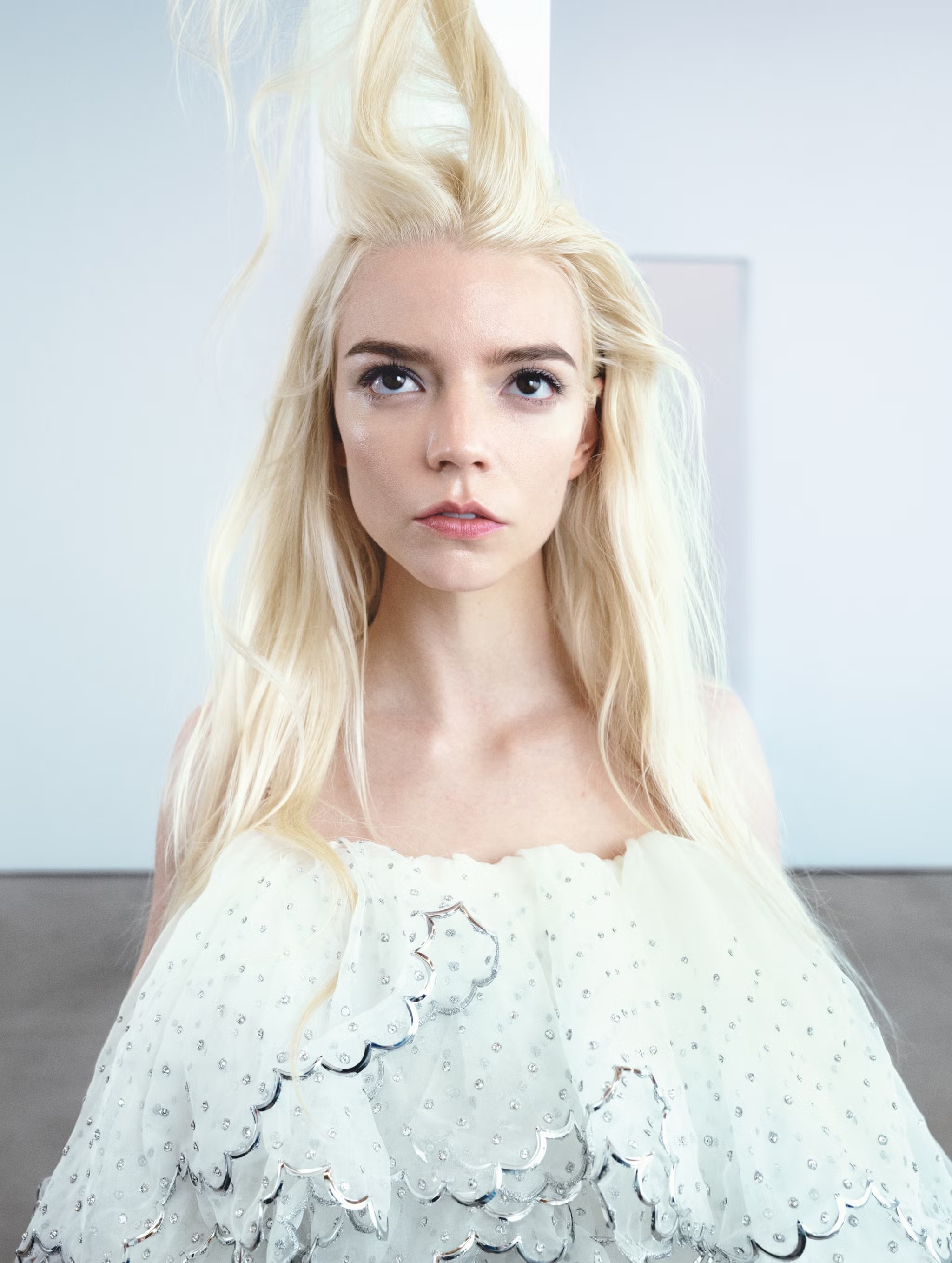 Anya Taylor-Joy with platinum blonde hair wearing a white textured dress against a light background for an Elle UK editorial