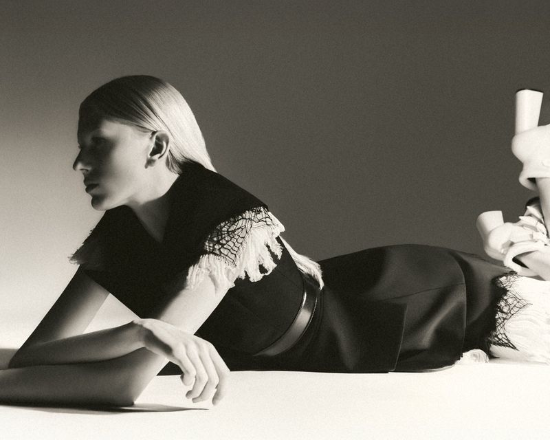 Monochrome fashion shot of a blonde woman in a black dress with lace, lying on her side with her head turned in a photo studio.