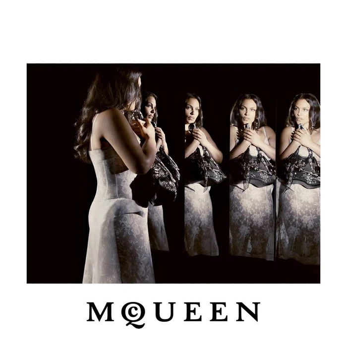 Paloma Elsesser in a white lace dress reflected in mirrors against a black backdrop for McQueen Fall 2026.