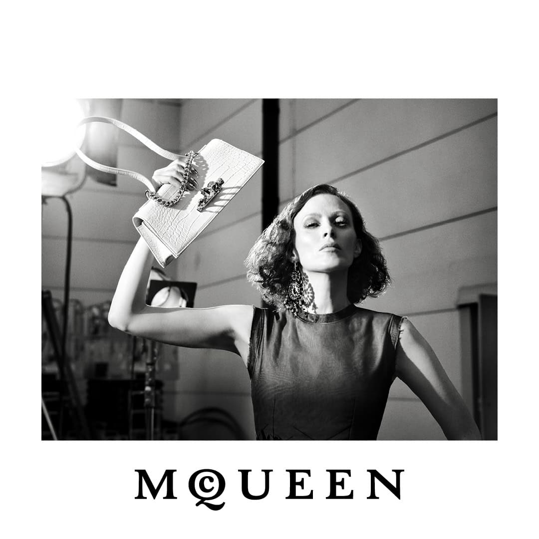 Black and white portrait of a model holding a white structured McQueen handbag aloft against a studio setting.