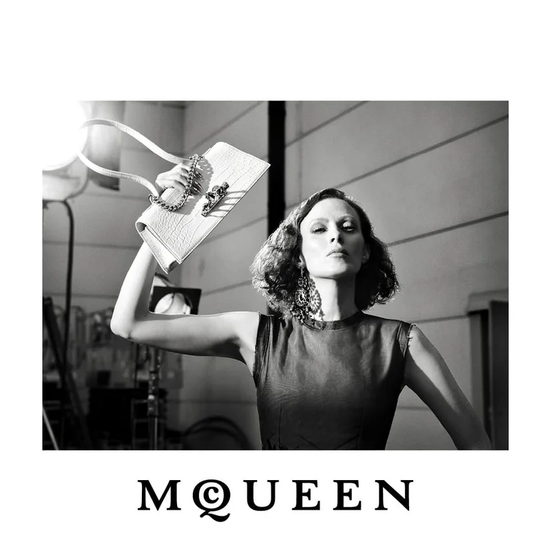 Black and white portrait of a model holding a white structured McQueen handbag aloft against a studio setting.