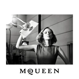 Black and white portrait of a model holding a white structured McQueen handbag aloft against a studio setting.