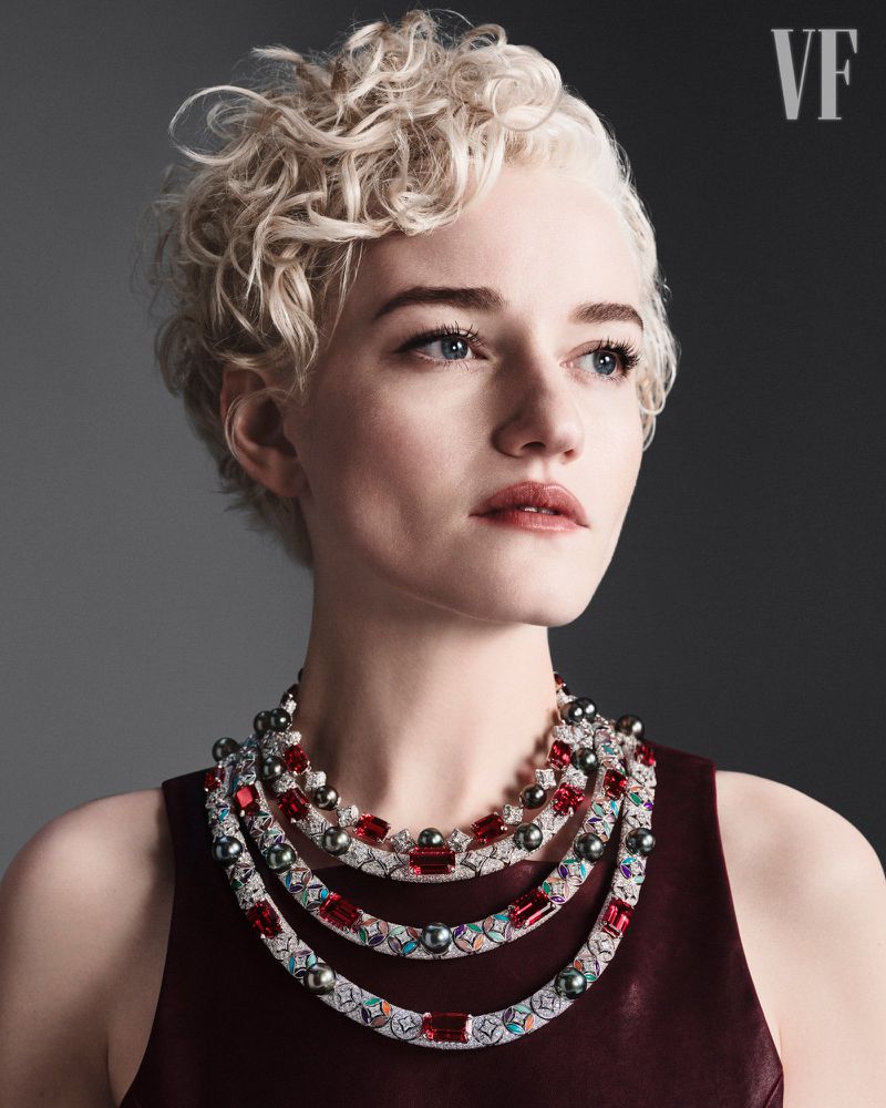 Portrait of a fair-skinned adult woman with short blonde curly hair wearing a burgundy sleeveless top and a layered pearl and ruby necklace.