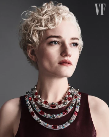 Portrait of a fair-skinned adult woman with short blonde curly hair wearing a burgundy sleeveless top and a layered pearl and ruby necklace.