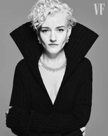 Black and white portrait of a blonde woman in a black, deep V-neck sweater and statement diamond necklace with diamond stud earrings.