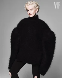 Julia Garner wearing an oversized black fuzzy knit sweater and knee-cutout leggings against a grey studio backdrop.