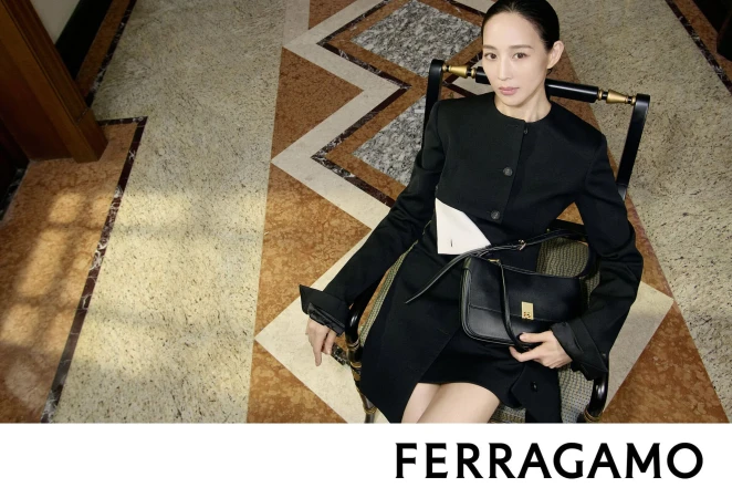 Ning Chang in a black tailored dress holding a black leather handbag while seated in a chair on a geometric marble floor.