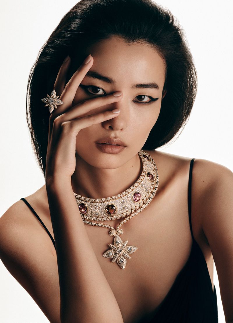 Close-up of a stylish Asian woman wearing an elegant diamond necklace and ring, in a bright studio setting for a jewelry advertisement.
