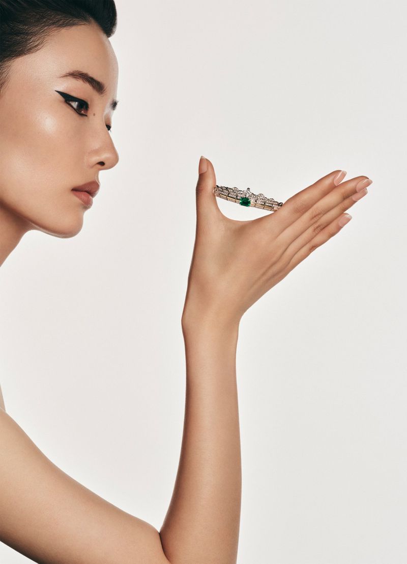Elegant Asian woman holds jeweled bracelet against a white background in a beauty or jewelry advertisement.