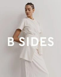 Model Aliza Jarmon wearing an off-white t-shirt and tied wrap skirt against a neutral backdrop with B SIDES text overlay.