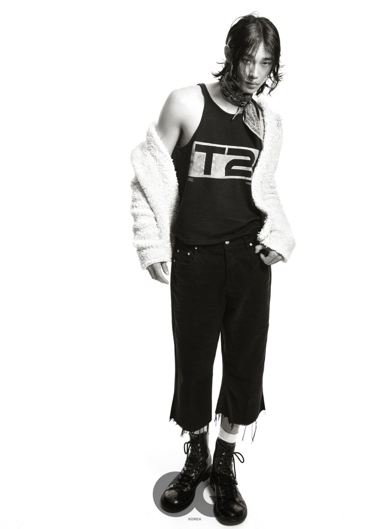 Model Taemin Park standing in a graphic tank top, cropped black pants, boots, and draped off-shoulder white fleece on a white backdrop.