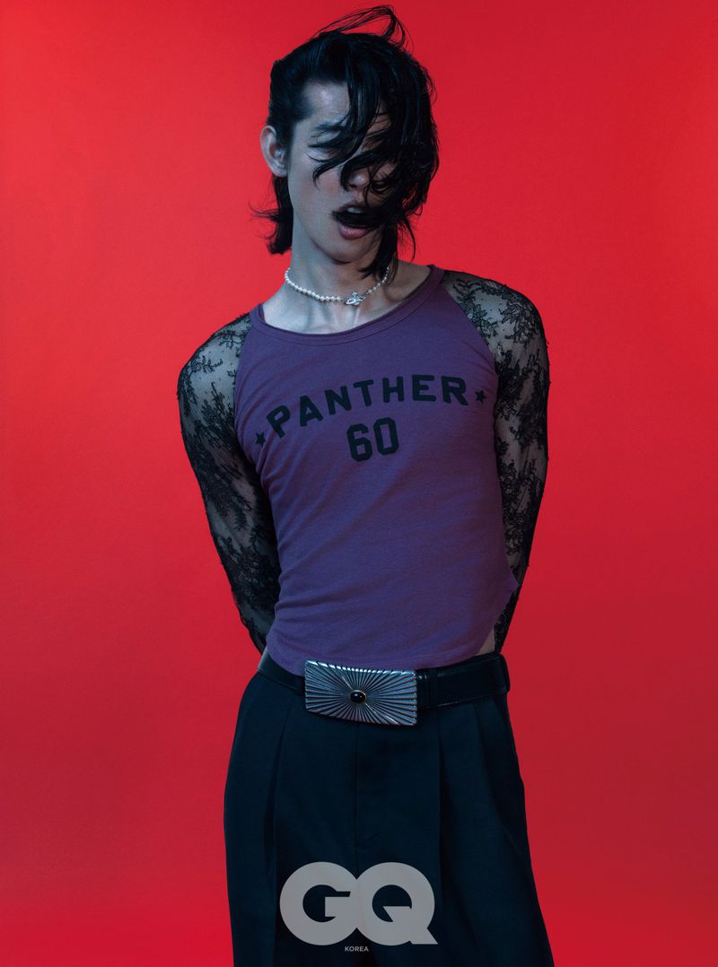 Model Taemin Park in a purple Panther graphic top with sheer black lace sleeves and dark trousers against a red studio backdrop.