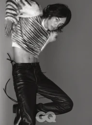 Model Taemin Park wearing a cropped striped sweater and black lace-up leather pants against a grey studio backdrop for GQ Korea.
