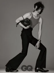 Model Taemin Park in high-waisted flared black trousers, sleeveless tank top, and heeled boots holding a black clutch bag.