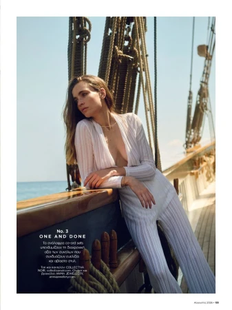 Model in white ribbed jumpsuit leaning against a wooden ship railing on the ocean for Harper's Bazaar Greece
