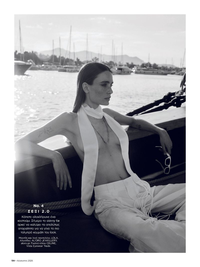 Monochrome fashion editorial image of a model wearing white trousers and scarf on a boat with a marina background.