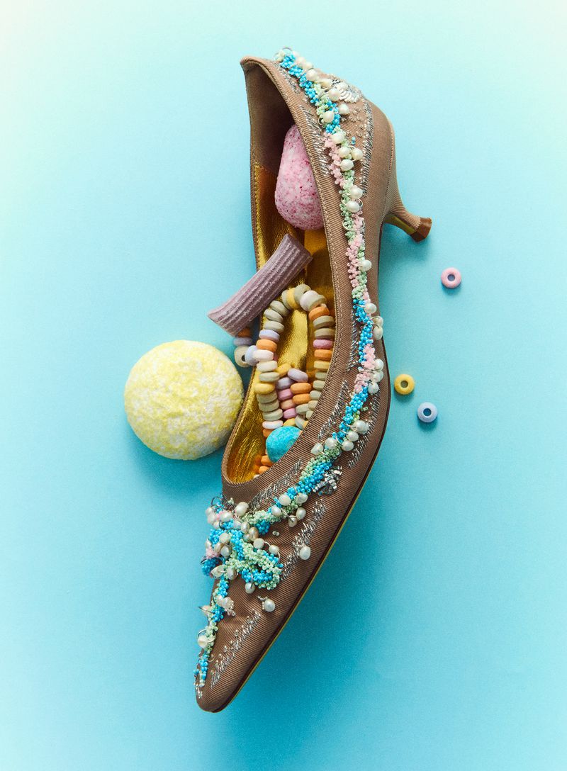 Embellished pointed-toe kitten heel filled with assorted pastel candies against a soft light blue background.