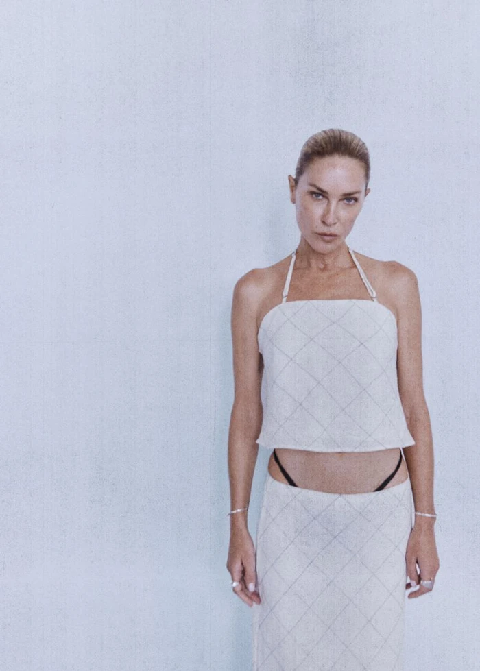 Erin Wasson wearing an off-white grid-patterned halter top and matching low-rise skirt against a pale studio backdrop.