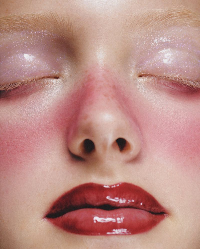 Close-up portrait of a woman's face featuring glossy red lips, pink blush, and shimmering light pink eyeshadow for beauty advertising.