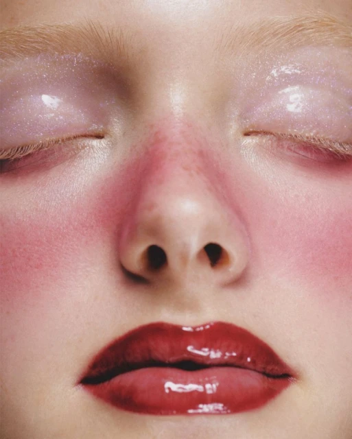 Close-up portrait of a woman's face featuring glossy red lips, pink blush, and shimmering light pink eyeshadow for beauty advertising.