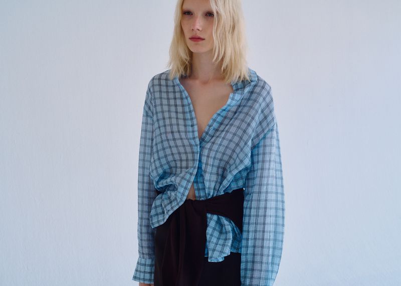Model Ivy Stewart in an oversized blue plaid shirt against a plain white studio backdrop.