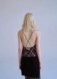 Model Ivy Stewart seen from behind wearing an open back criss-cross strap plaid top and dark wrap against a plain studio background.