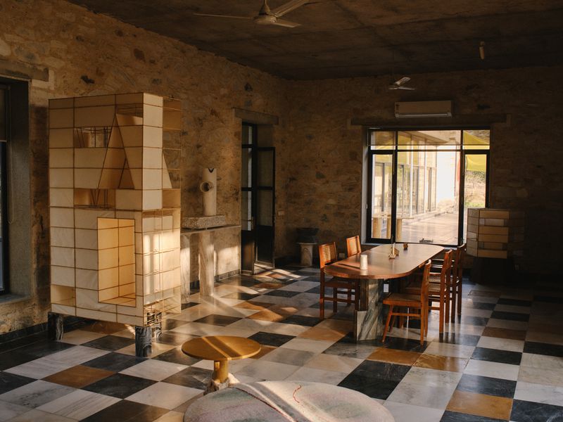 A rustic interior featuring a checkerboard floor, a modular wooden shelving unit, and a long dining table with wooden chairs.