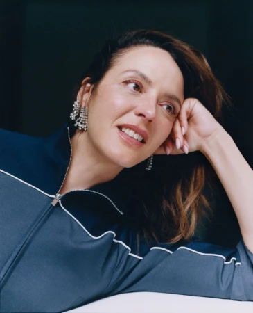 Close-up studio portrait of an adult woman with dark hair and chandelier earrings, wearing a navy blue track jacket, looking off camera.