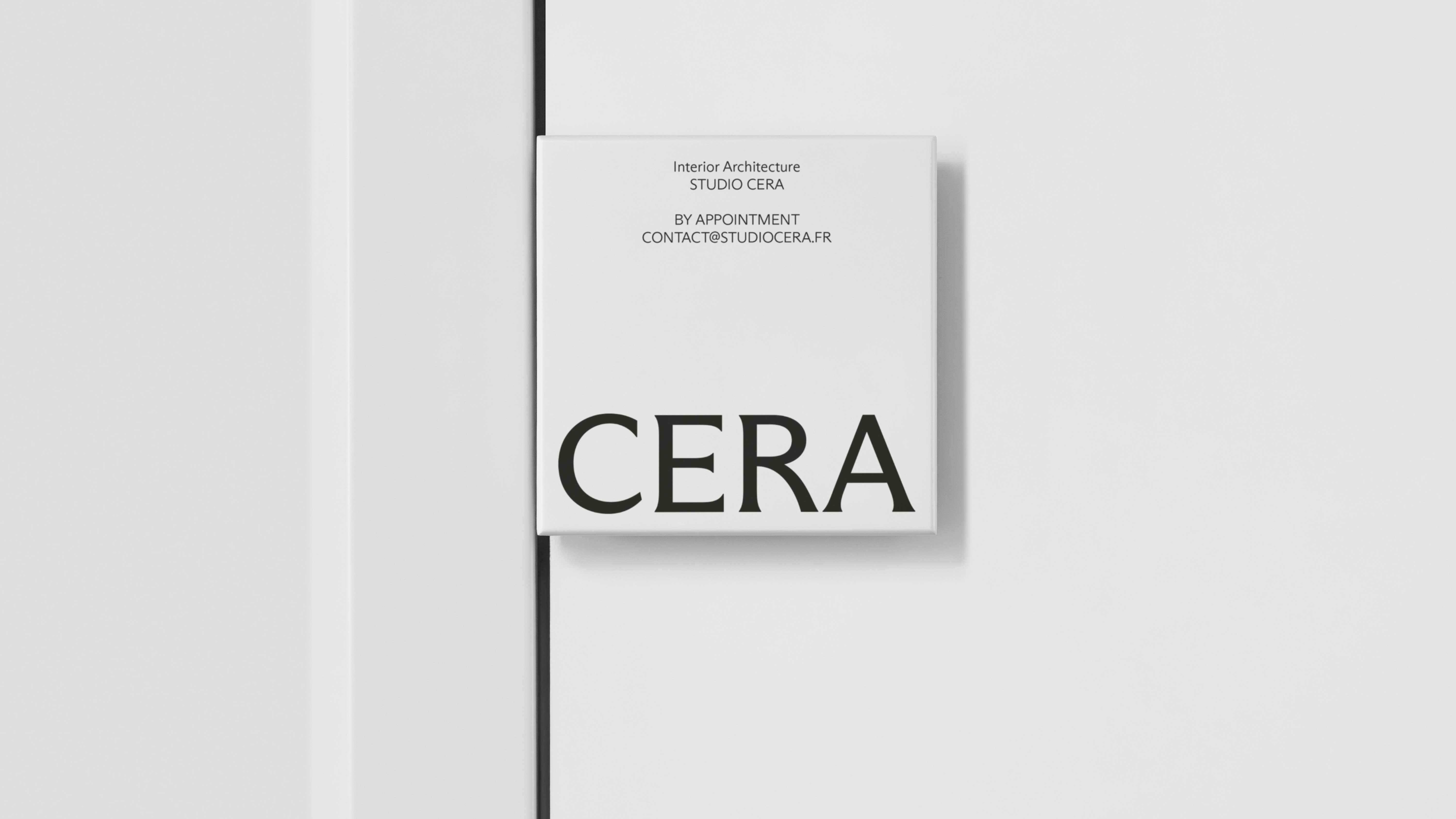 Square white Studio Cera door signage plaque with black typography mounted beside a minimalist white door frame.