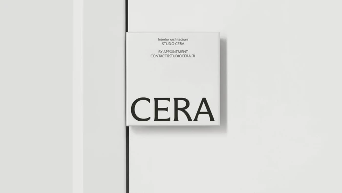 Square white Studio Cera door signage plaque with black typography mounted beside a minimalist white door frame.