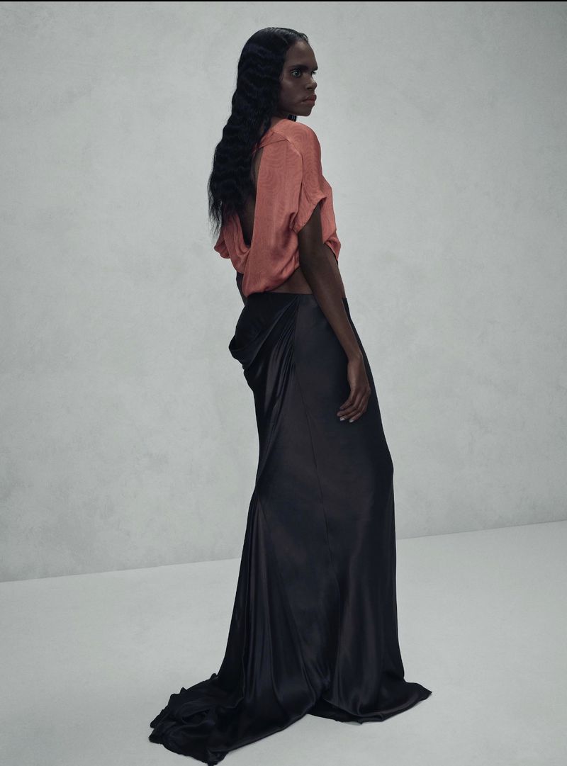 Fashion shot of a single model with long wavy hair in a peach top and black gown against a neutral backdrop in a studio environment.