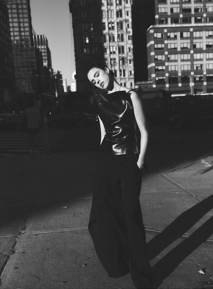 Black-and-white street-style fashion shot of a young woman in a black top and wide-leg pants posing in a city with tall buildings.